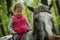 Girl enjoying horseback riding in the woods, young pretty girl with blond curly hair on a horse with backlit leaves