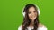 Girl enjoys music through headphones and sing along. Green screen. Close up