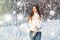 Girl enjoys the snow falls. Young woman in a knitted shape is drinking tea in the forest during a snowfall. Toned photo