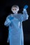 Girl examines a test tube with biomaterial. Young woman in protective clothing. On the face of a protective medical mask