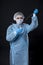 Girl examines a test tube with biomaterial. Young woman in protective clothing. On the face of a protective medical mask. A drop