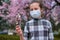 Girl with a face mask is in the city outdoor, blooming trees, spring season, flowering time - concept of allergies and health