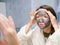 The girl in the face mask looks in the mirror displeased. Cosmetic black mask. Woman brings beauty to her face, gets rid of black