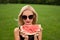 The girl falls in love on the field in photochromic glasses in the hand holding a slice of watermelon black hat from behind a