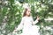 Girl in fashion dress pose at green tree. Little child with long blond hair outdoor. Kid model with fresh face skin in