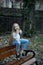 Girl in fashionable jeans sit on bench, fashion. Small child with long blond hair, hairstyle outdoor beauty. Baby beauty