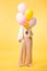 Girl in faux fur jacket holding balloons in front of face on yellow background