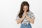 Girl feeling timid, laughing over funny joke on date. Studio shot of cheerful good-looking woman in striped t-shirt