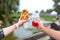 The girl and fella during the walk holds in hands a paper cup with a Belgian waffle and fresh drink on a background of green park