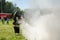 Girl in fireman uniform extinguishes burning tire on training
