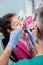 Girl with on the first dental visit. Senior pediatric dentist with nurse treating patient teeth at the dental office