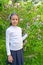 The girl first grader stands near the blossoming veygela in the park