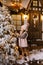 A girl of five or six years in winter pink clothes and ugg boots stands near the Christmas tree and decorates it with balls on the