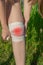 Girl fixes a bandage on an injured knee in the fresh air on a lawn. The injury site is highlighted in red