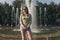 Girl with flowing hair in short shorts and sunglasses is standing in the fountain