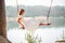 A girl in the forest swinging on a swing. Rope swing on a forest lake. Barefoot girl in a white dress with long hair