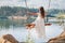 A girl in the forest swinging on a swing. Rope swing on a forest lake. Barefoot girl in a white dress with long hair