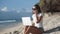 Girl freelancer in sunglasses works on beach with laptop and talks on phone