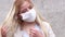 Girl in front of a gray wall puts on a white medical mask