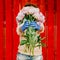A girl in front of a red fence in protective gloves holds out a bunch of peonies.