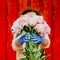 A girl in front of a red fence in protective gloves holds out a bunch of peonies.
