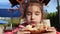 Girl is funny and eats pizza with an appetite in a street cafe in an open-air park. Street food, family time, walking