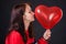 The girl gently touches large red heart-shaped balloon