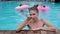 Girl gives an air kiss in pool on background girls with pink inflatable rings, friends swim into swimming-pool