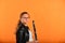 A girl with glasses in a black jacket holds a clarinet in her hands and looks into the camera, on a yellow background