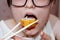 A girl with glasses puts a sushi roll in her mouth with chopsticks