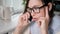 Girl with glasses talking intently on phone in kitchen, holding her head hands screen is reflected in lenses. Girl