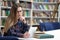 Girl in glasses working with tablet sitting in library. Student prefers to work with a tablet than books