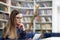 Girl in glasses working with tablet sitting in library. Student prefers to work with a tablet than books