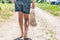 A girl goes to the store barefoot along the village road, bare feet, rear view. Eco-friendly reusable mesh bag, macrame.