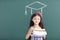 Girl in graduation cap with books standing before chalkboard