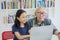 Girl and grandfather using laptop in library