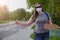 Girl in gray t-shirt, jeans, sunglasses and a medical mask with sign is staying near road, Humorous hitchhiking. Getting out of