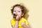 Girl with greed and appetite eats, bites delicious chocolate donut and raises finger up on yellow background