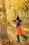 Girl in the guise of a witch sits astride a broomstick in the forest between the autumn yellow foliage of trees on Halloween