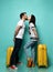 Girl and guy in casual clothes are going to kiss each other, posing with yellow suitcases, standing sideways on blue background