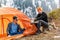 Girl and a guy at a stop with a tourist tent drinking tea or coffee on a background of forest snow-capped mountains