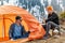 Girl and a guy at a stop with a tourist tent drinking tea or coffee on a background of forest snow-capped mountains. A walking met