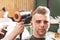 Girl hairdresser sprays spray and dries hair with a hairdryer to a young guy sitting in a chair in a barbershop