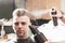 Girl hairdresser sprays spray and dries hair with a hairdryer to a young guy sitting in a chair in a barbershop