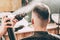 Girl hairdresser sprays spray and dries hair with a hairdryer to a young guy sitting in a chair in a barbershop