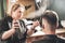 Girl hairdresser sprays spray and dries hair with a hairdryer to a young guy sitting in a chair in a barbershop