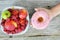 Girl hand holding an appetising glazed donut near a bowl of fresh ripe fruits on wooden table