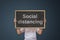 Girl hand holding black board sign with text Social distancing