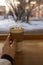 The girl hand touches a white glass of coffee on top sprinkled with marshmallows standing on a reco-collar. Vertical photo