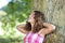 Girl With Hands Behind Head Leaning On Tree Trunk